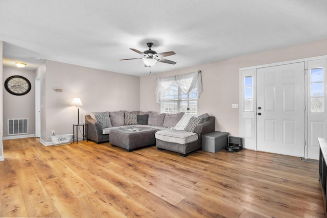 living room with ceiling fan, a textured ceiling, and light hardwood / wood-style floors