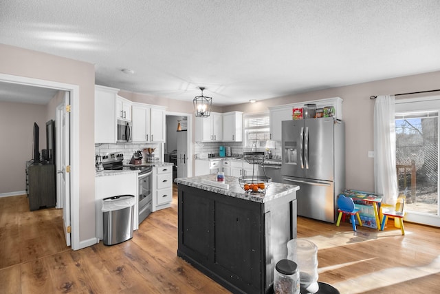 kitchen with appliances with stainless steel finishes, white cabinetry, hanging light fixtures, a kitchen island, and light wood-type flooring