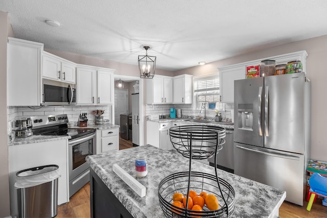 kitchen with a kitchen island, appliances with stainless steel finishes, decorative light fixtures, white cabinets, and light stone counters