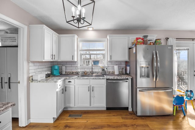 kitchen with appliances with stainless steel finishes, sink, white cabinets, dark hardwood / wood-style flooring, and hanging light fixtures