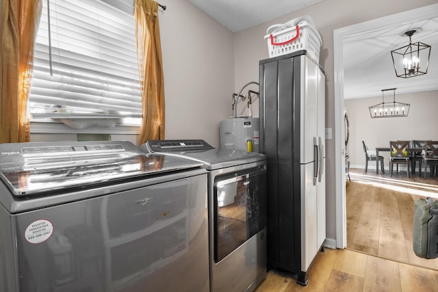 washroom with electric water heater, light hardwood / wood-style floors, independent washer and dryer, and a chandelier