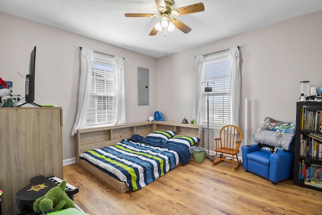 bedroom featuring electric panel, hardwood / wood-style floors, multiple windows, and a textured ceiling