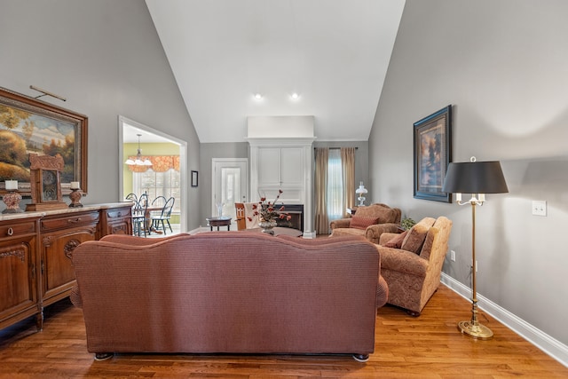 living room with a notable chandelier, high vaulted ceiling, and light hardwood / wood-style flooring