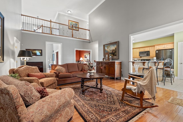 living room featuring crown molding, light hardwood / wood-style flooring, and a high ceiling