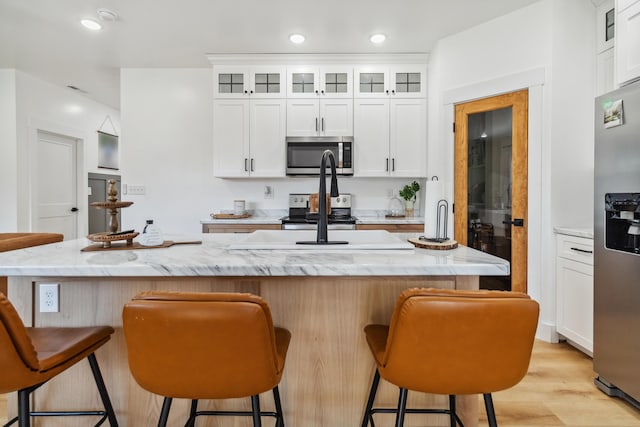 kitchen with appliances with stainless steel finishes, a breakfast bar, a center island with sink, and white cabinets