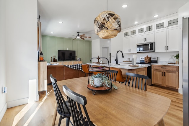 kitchen with decorative light fixtures, light hardwood / wood-style flooring, an island with sink, stainless steel appliances, and white cabinets