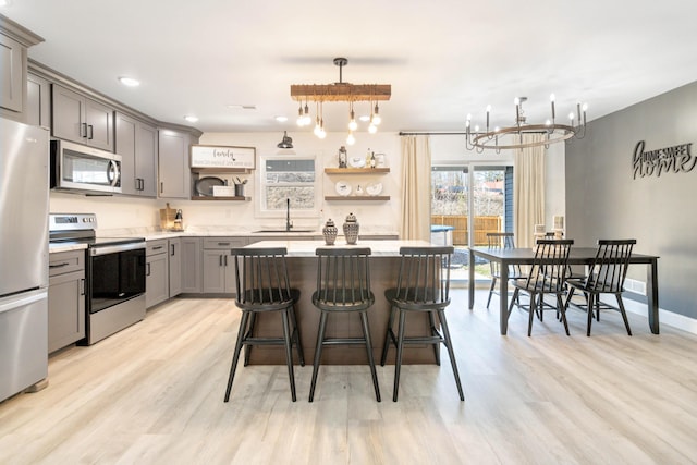 kitchen featuring appliances with stainless steel finishes, decorative light fixtures, sink, a kitchen bar, and light wood-type flooring