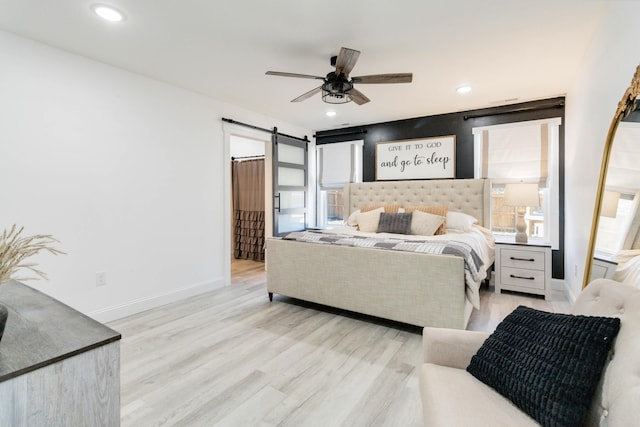 bedroom with a barn door, ceiling fan, and light wood-type flooring