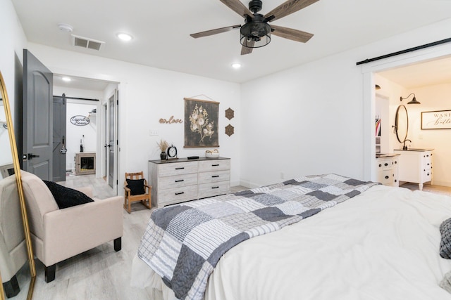 bedroom featuring light hardwood / wood-style flooring, a barn door, and ceiling fan