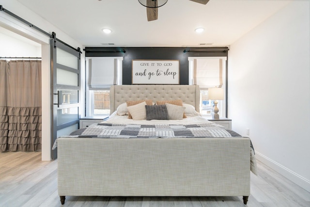 bedroom with light hardwood / wood-style floors, a barn door, and ceiling fan