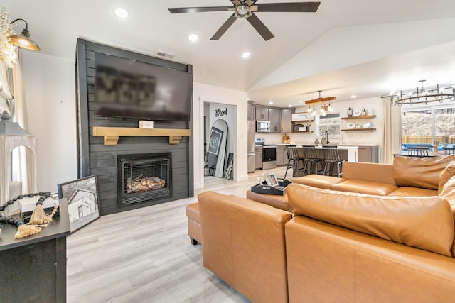 living room featuring vaulted ceiling, a fireplace, sink, ceiling fan, and light wood-type flooring