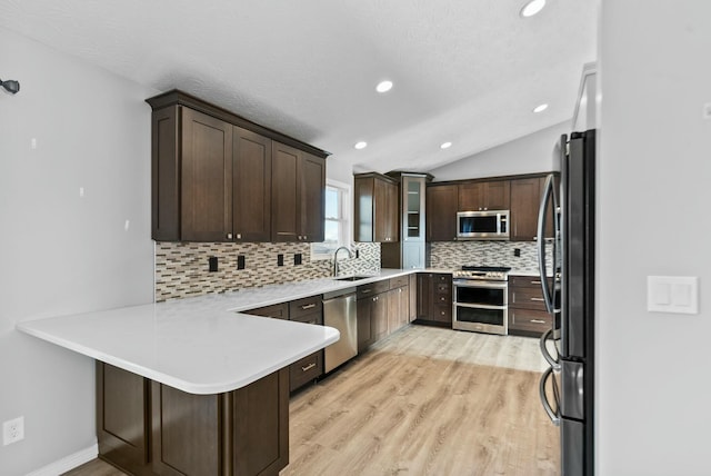 kitchen featuring vaulted ceiling, backsplash, kitchen peninsula, stainless steel appliances, and light hardwood / wood-style flooring