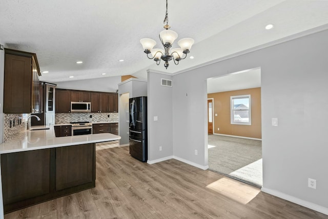 kitchen with sink, appliances with stainless steel finishes, hanging light fixtures, tasteful backsplash, and kitchen peninsula