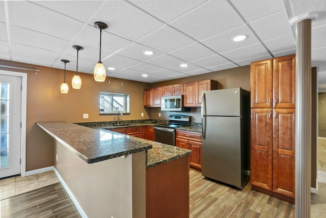 kitchen featuring decorative light fixtures, dark stone counters, kitchen peninsula, stainless steel appliances, and light hardwood / wood-style flooring