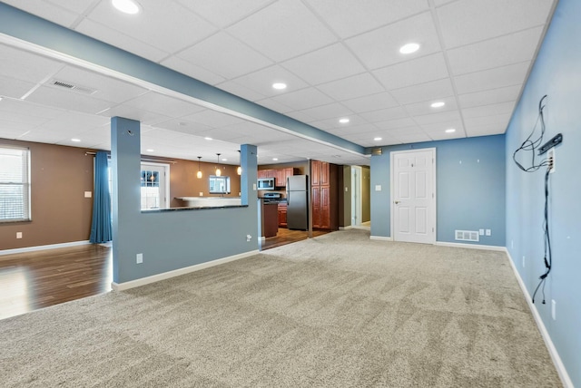 unfurnished living room featuring a wealth of natural light, dark carpet, and a drop ceiling