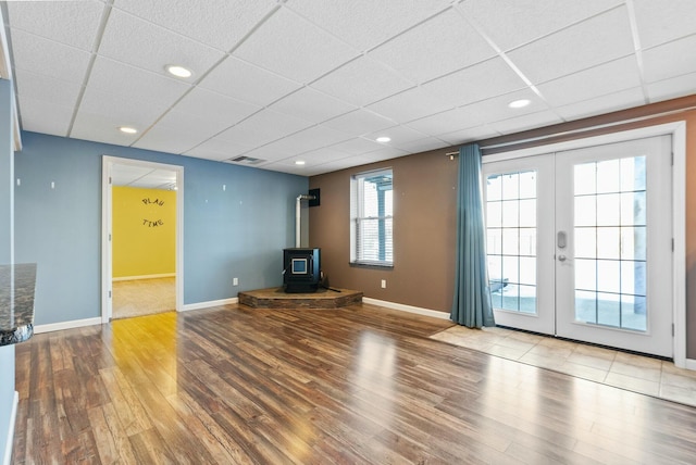 unfurnished living room featuring french doors, a paneled ceiling, wood-type flooring, and a wood stove