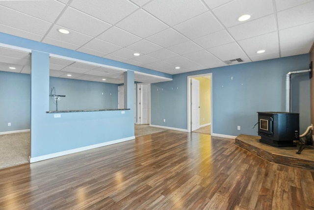 unfurnished living room with a paneled ceiling, a wood stove, and hardwood / wood-style floors