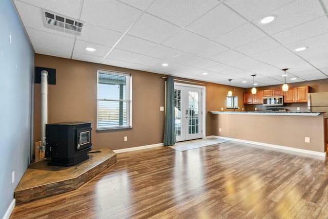 unfurnished living room featuring a paneled ceiling, a wood stove, hardwood / wood-style floors, and french doors