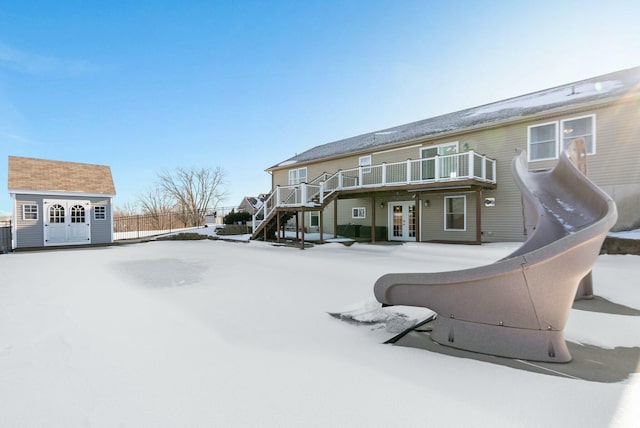 snow covered back of property with a garage, a wooden deck, an outbuilding, and french doors