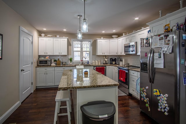 kitchen with a kitchen island, appliances with stainless steel finishes, pendant lighting, white cabinetry, and light stone counters