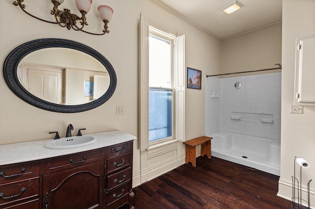 bathroom with hardwood / wood-style flooring, crown molding, an inviting chandelier, tiled shower, and vanity