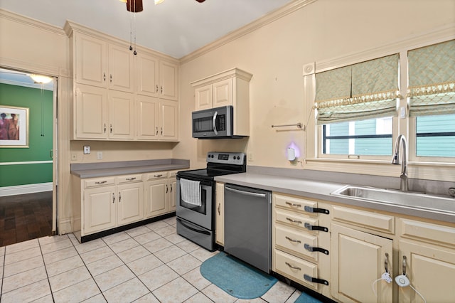 kitchen with sink, crown molding, light tile patterned floors, appliances with stainless steel finishes, and cream cabinets