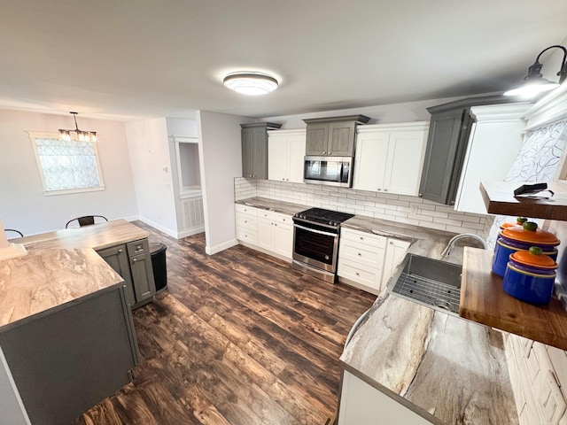 kitchen with appliances with stainless steel finishes, gray cabinetry, dark hardwood / wood-style flooring, decorative backsplash, and hanging light fixtures