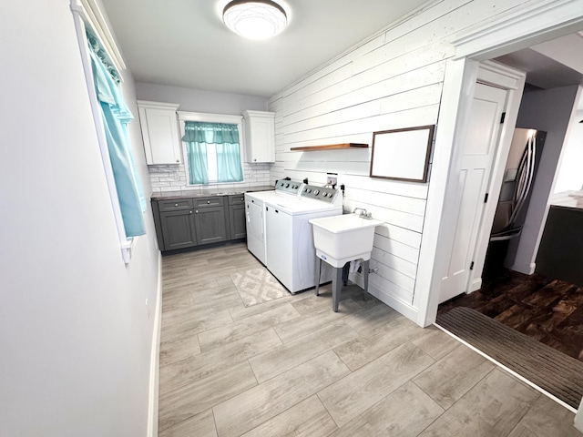 clothes washing area with cabinets, washer and dryer, sink, and light hardwood / wood-style flooring