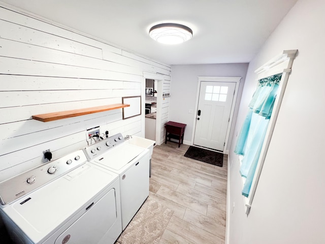 washroom with washing machine and dryer, light wood-type flooring, and wooden walls