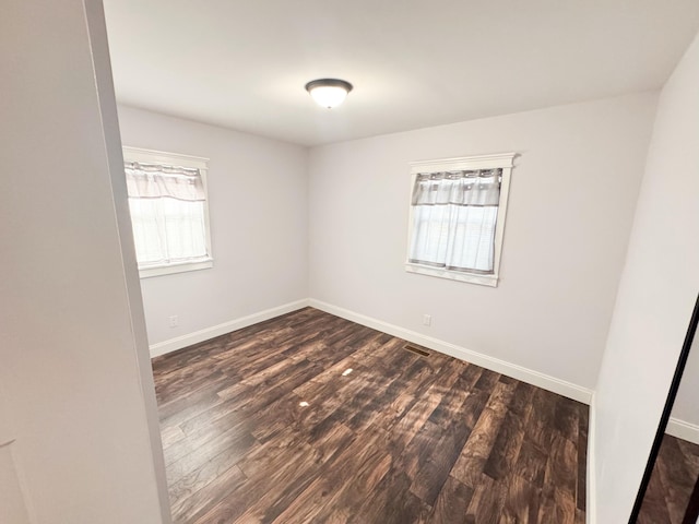 empty room with a healthy amount of sunlight and dark hardwood / wood-style flooring