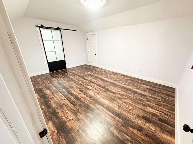 empty room featuring dark wood-type flooring, lofted ceiling, and a barn door