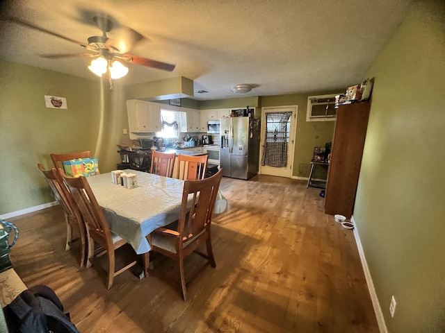 dining room with a textured ceiling, wood finished floors, a ceiling fan, baseboards, and a wall mounted air conditioner