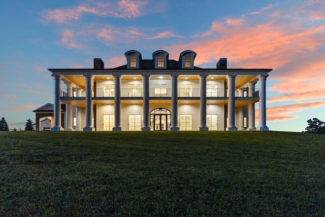 back house at dusk featuring a balcony and a yard