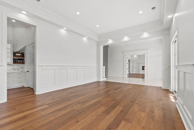 unfurnished living room featuring bar, crown molding, wood-type flooring, and decorative columns