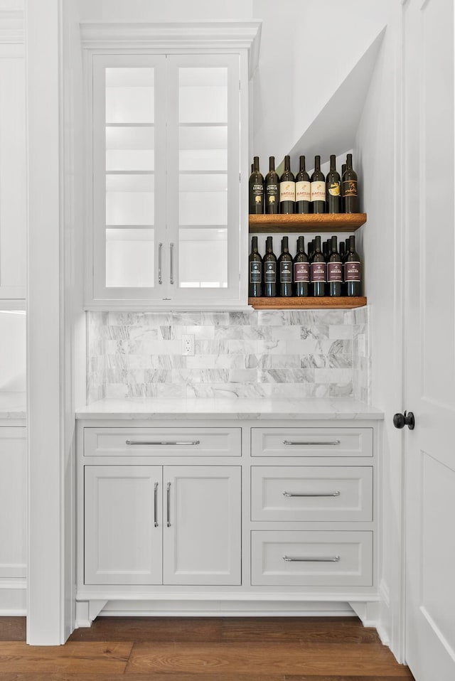 bar featuring backsplash, dark wood-type flooring, light stone counters, and white cabinets