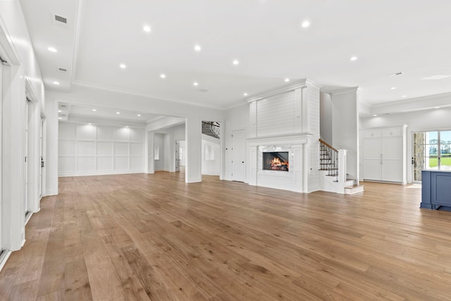 unfurnished living room with ornamental molding, a large fireplace, and light hardwood / wood-style floors