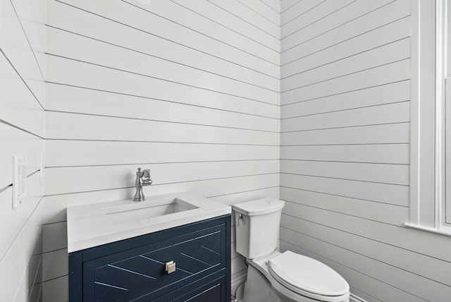 bathroom featuring wooden walls, vanity, and toilet