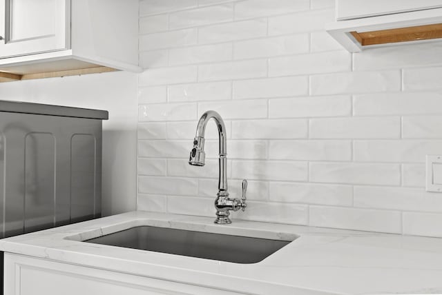 interior details featuring light stone countertops, sink, and white cabinets