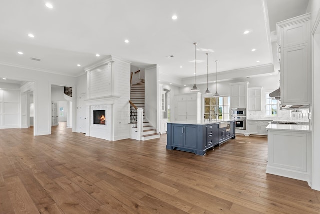 kitchen with wall chimney exhaust hood, hanging light fixtures, a center island with sink, a fireplace, and white cabinets