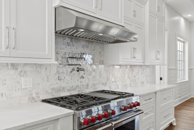 kitchen featuring white cabinetry, high end range, light stone counters, ventilation hood, and decorative backsplash