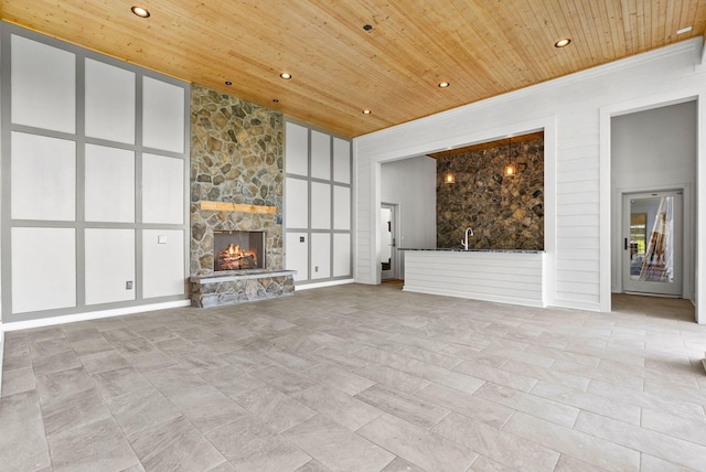 unfurnished living room featuring a high ceiling, a stone fireplace, and wood ceiling