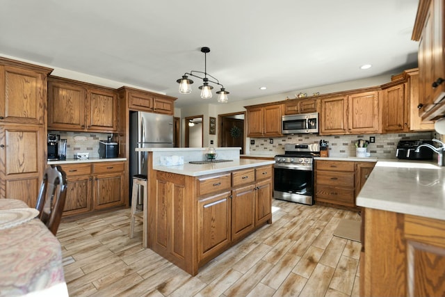 kitchen featuring decorative light fixtures, tasteful backsplash, a center island, light hardwood / wood-style floors, and stainless steel appliances