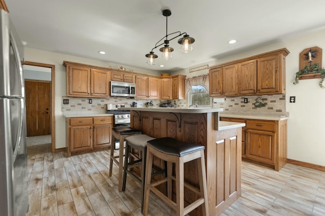 kitchen with appliances with stainless steel finishes, hanging light fixtures, a kitchen island, and light wood-type flooring