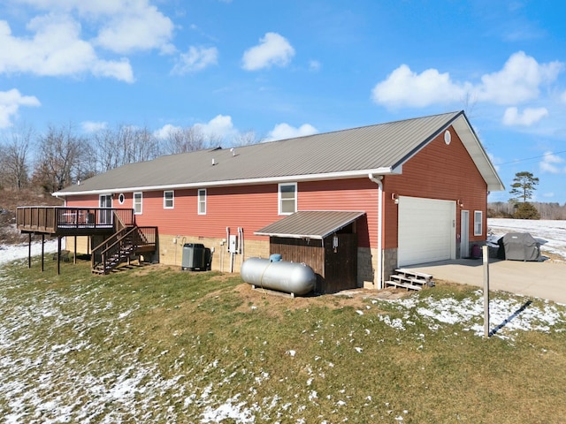 snow covered property featuring a garage, a wooden deck, central AC unit, and a lawn