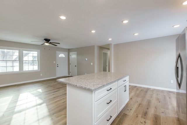 kitchen with stainless steel refrigerator, white cabinetry, a center island, light stone countertops, and light hardwood / wood-style flooring