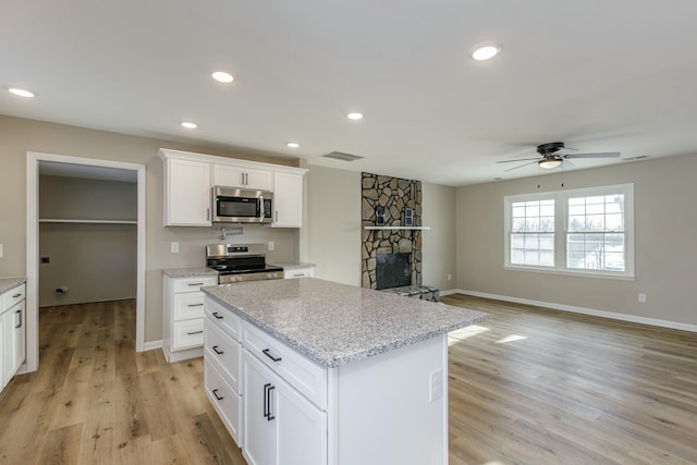 kitchen with appliances with stainless steel finishes, white cabinetry, light stone counters, light hardwood / wood-style floors, and a kitchen island