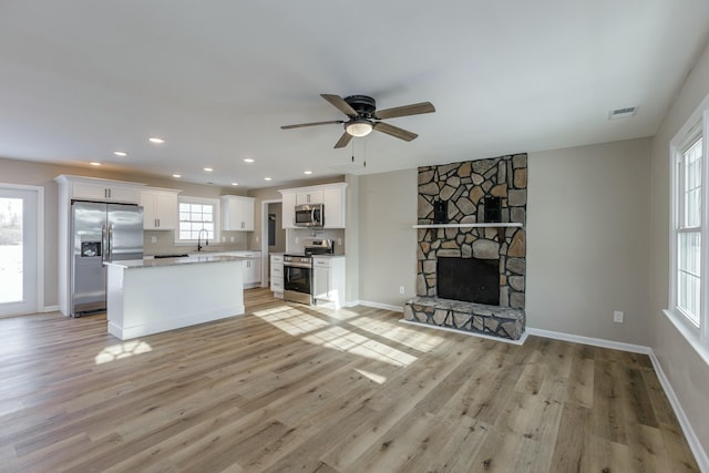 kitchen featuring appliances with stainless steel finishes, a kitchen island, a fireplace, light hardwood / wood-style floors, and white cabinets