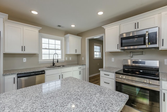 kitchen with sink, light stone countertops, white cabinets, and appliances with stainless steel finishes