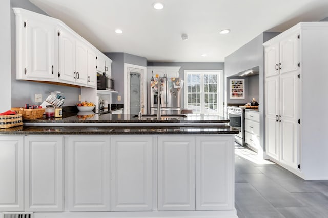 kitchen with dark stone countertops, stainless steel appliances, kitchen peninsula, and white cabinets