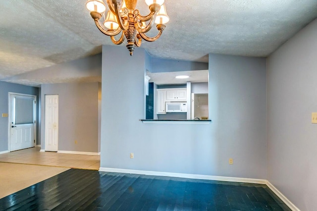 spare room featuring lofted ceiling, hardwood / wood-style floors, a textured ceiling, and a chandelier